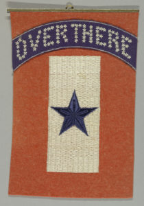Red wool felt banner embroidered with a blue star on a white rectangle, with the words "Over There" embroidered in white on a blue arch above.
