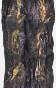 Length of textile with a dark, shiny surface and overall random creasing. Areas of color are revealed when the creases are unfolded.
