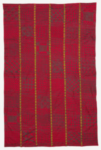 Six strips of bright red cotton stamp-printed in dark brown/black in a variety of geometric symbols. The strips are joined by embroidery patterned in bands of black, blue, green, and yellow.