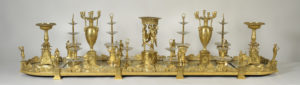 Magnificent golden table centerpiece with ornate classical motifs, such as the Three Graces, that provide architectural support for food stands.