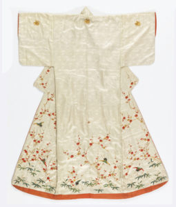 Woman's kimono of white satin with woven design of tiny lozenges, tortoises and phoenixes. Embroidered with silk threads in red, gold and green with cherry blossoms, pine branches, bamboo, phoenix and butterflies. Lined with red silk.