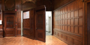 Verbal Description tour of The Carnegie Mansion. Image of the great hall interior walls. Deep wooden paneling covers a concealed door hinged slightly open. Scroll down for more information on the program.