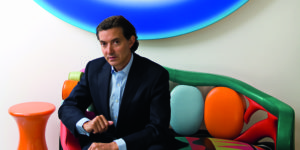 Design, Taste, and Influence: Conversation with David Gill. Image of David seated on a colorful sofa in front of a blue artwork. Scroll down for program details.