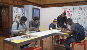 A group of teen boys sit around a work table experimenting with color combinations in the Process Lab installation Scholten & Baijings: Lessons from the Studio. Scroll down for more information about the exhibition.