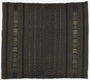 Image features a sarong with vertical stripes of white ikat-dyed patterning on an indigo ground. Scroll down to read the blog about this object.