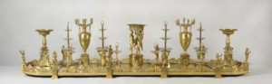 The surtout de table, a magnificent golden table centerpiece fit for royalty. Detailed ornaments, such as the Three Graces, provide architectural support for food stands.
