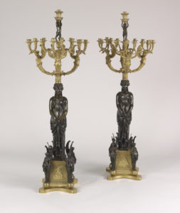 This image features two candelabra, featuring a standing female figure of patinated bronze supporting branched gilt-bronze candle arms, each arm in the form of a winged female figure; the branches are surmounted by a patinated putto/faun standing on a column and holding an urn-shaped bobeche; square gilt-bronze base with a scene of Europa and the bull; a patinated winged female term stands at each corner. The female figures stand on a gilt-bronze plinth. Please scroll down to read the blog post about this object.