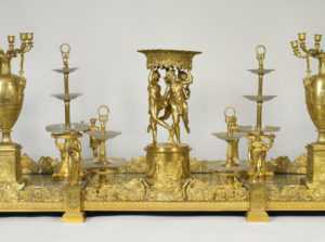 Detail view of surtout de table. In a magnificent golden centerpiece, sculptures of the Three Graces provide an architectural support for a food stand.
