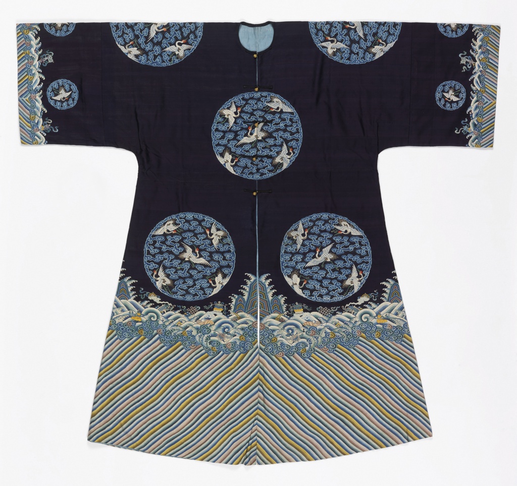 Image features: A robe of dark blue silk with a deep wave border at the bottom and sleeve hems. Tapestry-woven design of eight large circular medallions showing five white cranes with red crests and blue cloud bands. Lined with light blue silk. Please scroll down to read the blog post about this object.