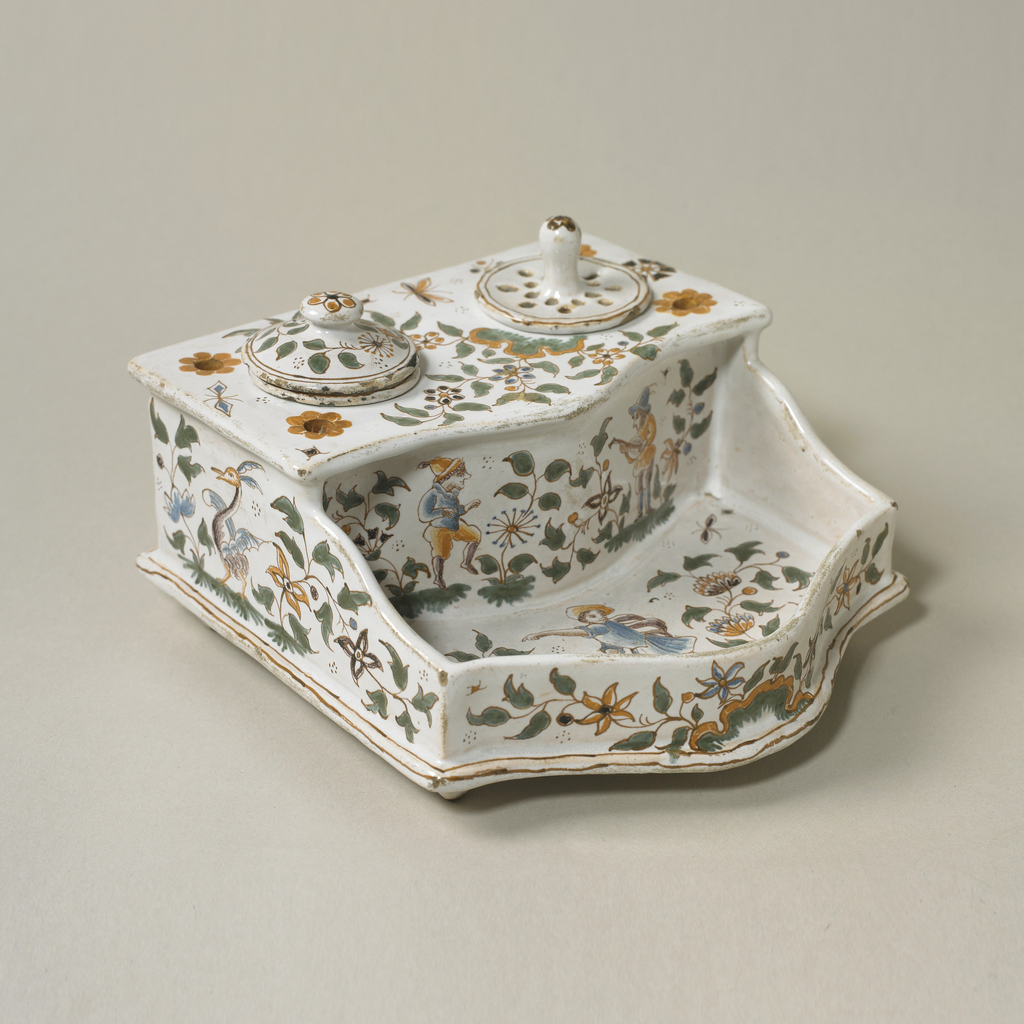 Image featues a shaped inkstand with inset inkpot and sander, each with a circular lid; green and ochre decoration of flowers, foliage, and figure. Please scroll down to read the blog post about this object.