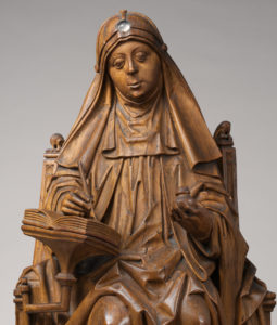 This image features a carved wood sculpture of St. Bridget of Sweden, seated, writing.