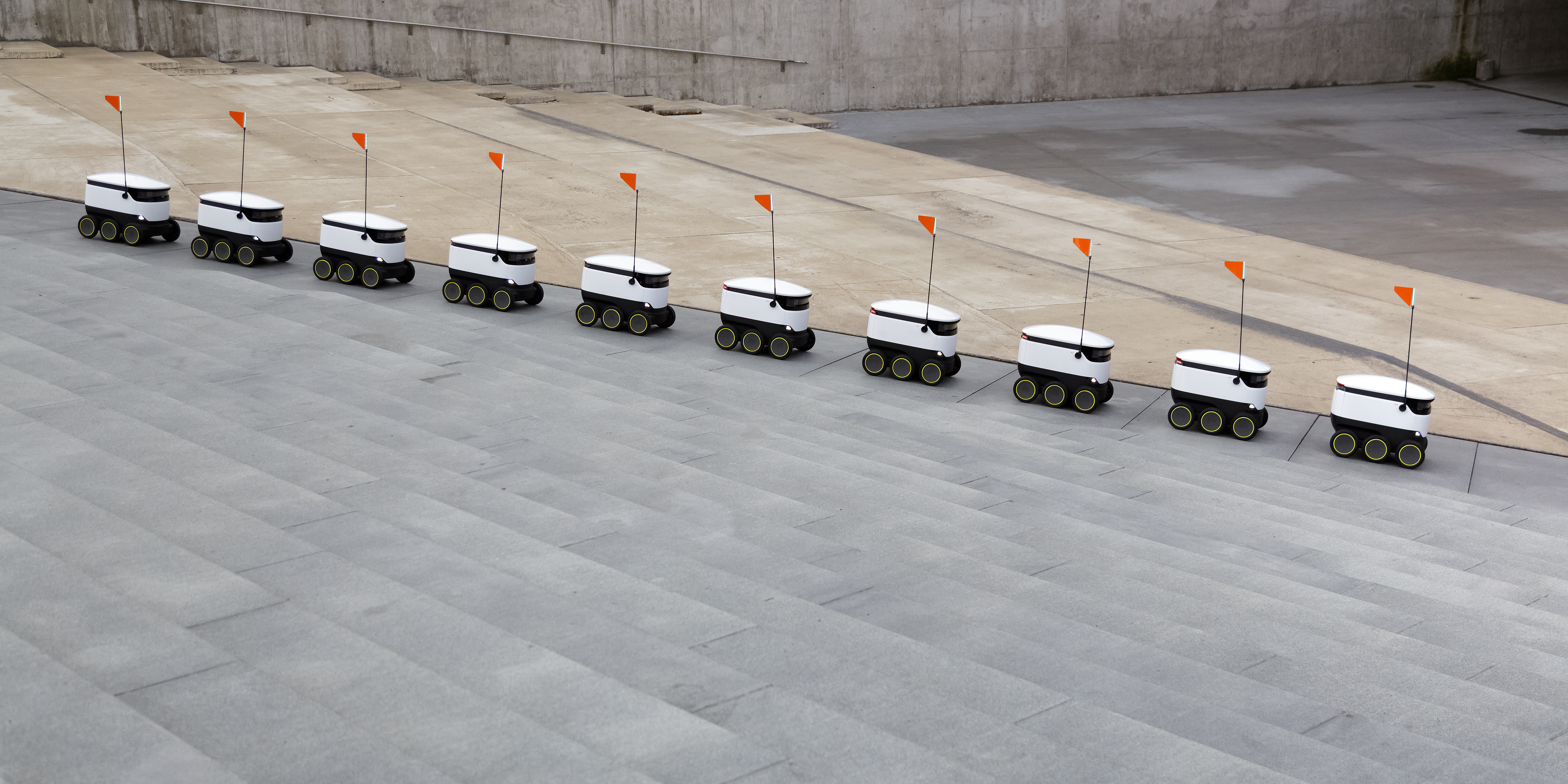 Verbal description tour of the road ahead. Image of a line of small white starship robots wheeling over tiled gray ground.