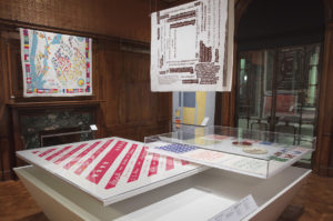 Photograph of textiles laid in display cases and hung vertically in a museum gallery.
