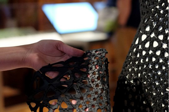 Close-up image of a hand holding a black plastic 3-D printed geometric material sample.