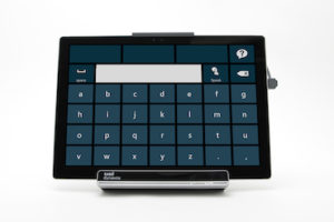 a rectangle black tablet with a large keyboard of blue keys and a narrow screen at top of the keyboard. The tablet is a hands-free mobile, computer access communication system now on view in a Cooper Hewitt installation of inclusive design at the World Economic Forum.