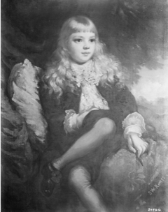 A vertical portrait of a young boy. He sits at center, looking slightly away from the viewer, his legs crossed with his right hand on his left thigh. He hair is long and wavy, and he is dressed in short pants, a frilly blouse, and a jacket—children's formalwear typical of the late nineteeth century. The background is a blurry mix of foliage and draped fabrics.