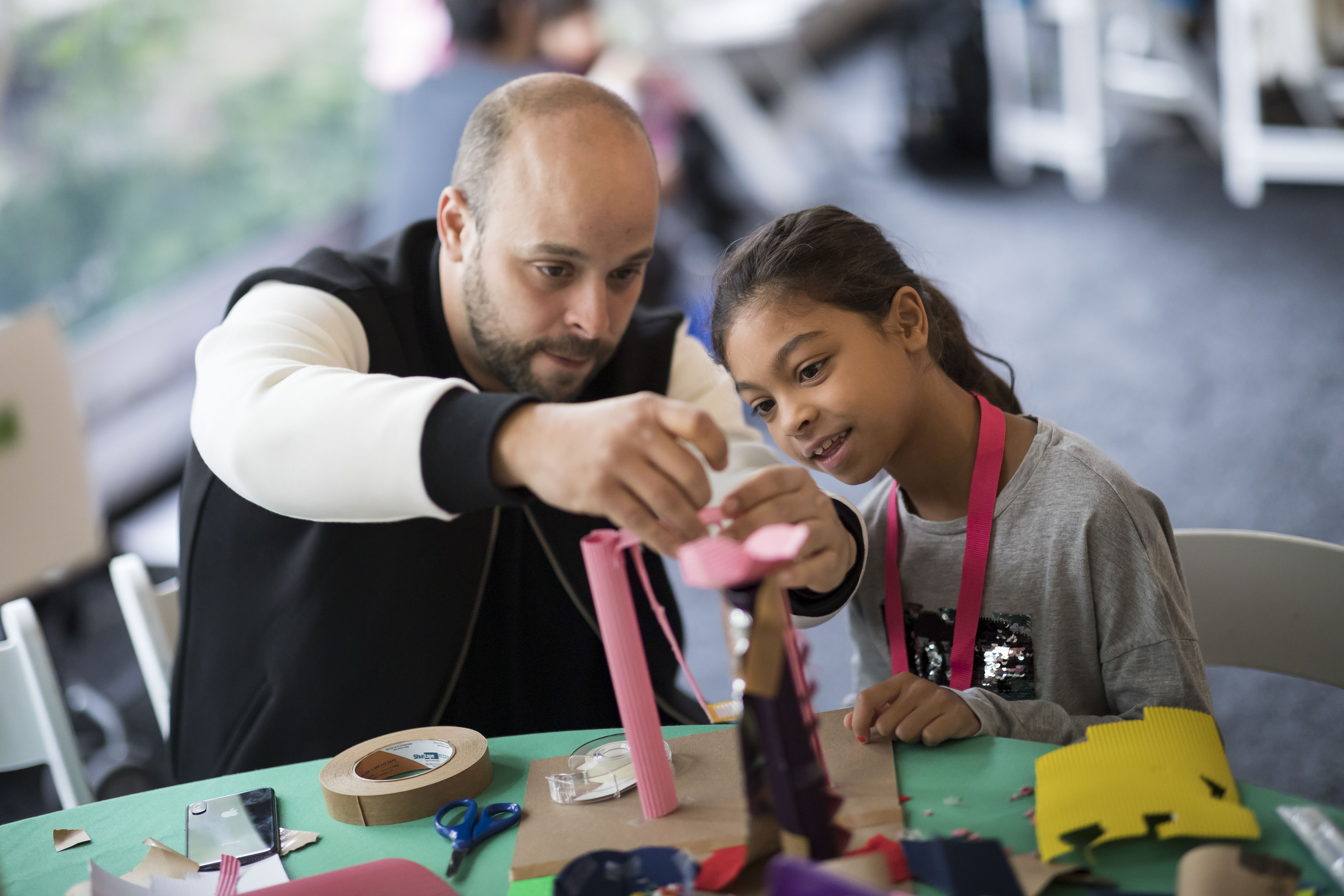 A man and a child work together on a three-dimensional design made from colorful paper