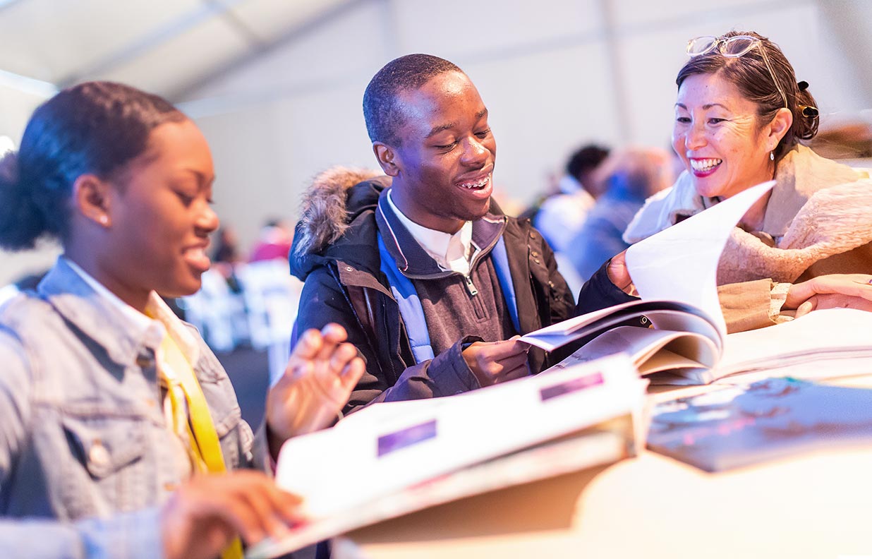 Three people seated at a table smile and look at books