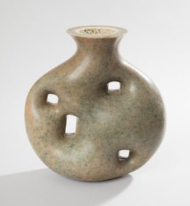 Mottled tan to gray-green plastic vase having a short neck and circular mouth, the roughly circular body molded with one rectangular and three irregular square openings.