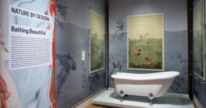 In the galleries of Cooper Hewitt, a white bathtub is on display. Surrounding the bathtub are three panels of a wallcovering that look like a water color painting of pink fish frolicking in a pale green sea. As a decorative touch from the Cooper Hewitt curators, the pattern of the wallpaper has been blown up and turned dark blue to show what the pattern would like like if it extended from floor to ceiling around the tub.