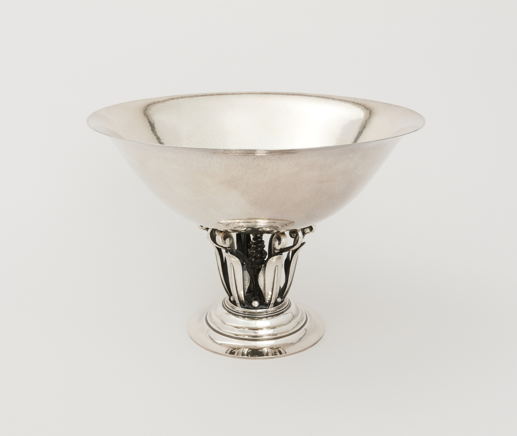 Image features a raised circular bowl with a wide rim supported by a center column composed of stylized curled leaves surrounding a cluster of grapes, all on a stepped circular foot. Please scroll down to read the blog post about this object.