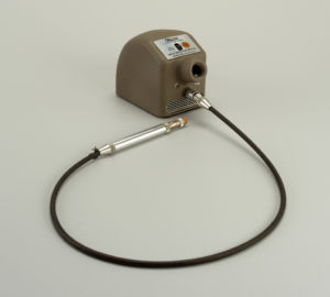 Image features brown metal unit housing electric motor, having on/off switch at top, circular projection at front with black cord below; pen-like metal "wand" holding cylindrical pink rubber eraser at end. Please scroll down to read the blog post about this object.