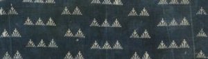 Image features dark blue fabric with small, closely spaced design of triangles joined in lines of two or three reserved in white.