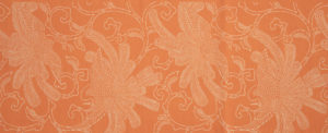 An orange piece of fabric with a white stenciled design of a peacocks