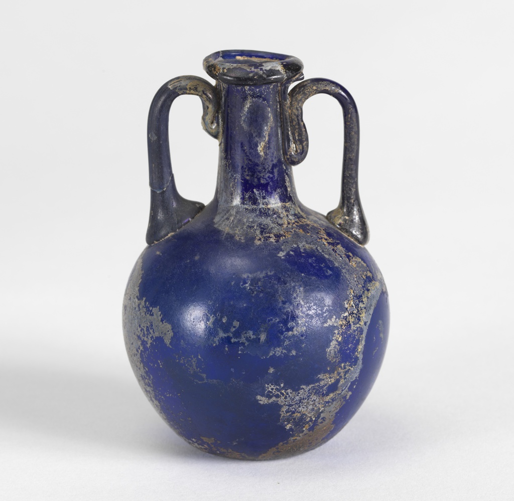 Round-bodied vase with two curved handles that flank a skinny cylindrical neck; it is cobalt blue–a deep medium blue