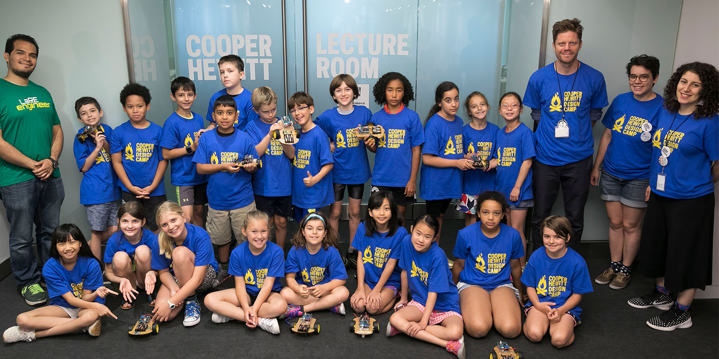 Large group of youths and four adults pose smiling, all wear bright blue T-shirts that say “COOPER HEWITT DESIGN CAMP”