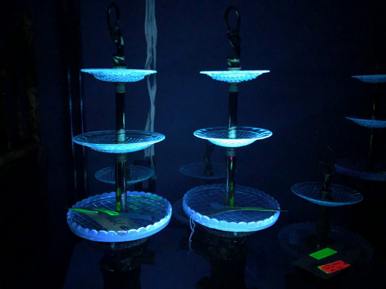 In general darkness, two towers (approximately two-feet high each) with three tiers of glass dishes glow blue under ultra-violet light.