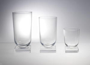 Image features three clear glass drinking glasses in graduated sizes, each one in the form of a cylinder with a curved base on a low square foot. Please scroll down to read the blog post about these objects.