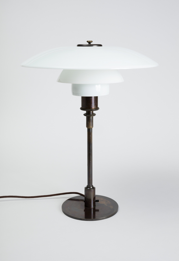 Image features a lamp with a three-tiered shade composed of three stacked glass circles of graduated sizes, all on a simple dark brown metal base consisting of a vertical rod on a circular foot. The lamp is topped by a circular dark metal screw-on cap. Please scroll down to read the blog post about this object.