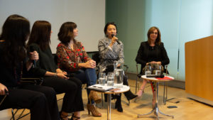 Image of panel discussion at Cooper Hewitt. 5 women with microphones on a stage, two small tables with glasses of water. Grace Jun is speaking, she holds the mic to her mouth.