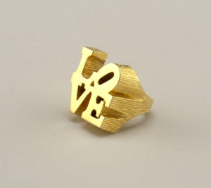 Image features a gold-toned ring with the capital letters L and O (on angle), stacked over the letters V and E, spelling out the word love. Please scroll down to read the blog post about this object.
