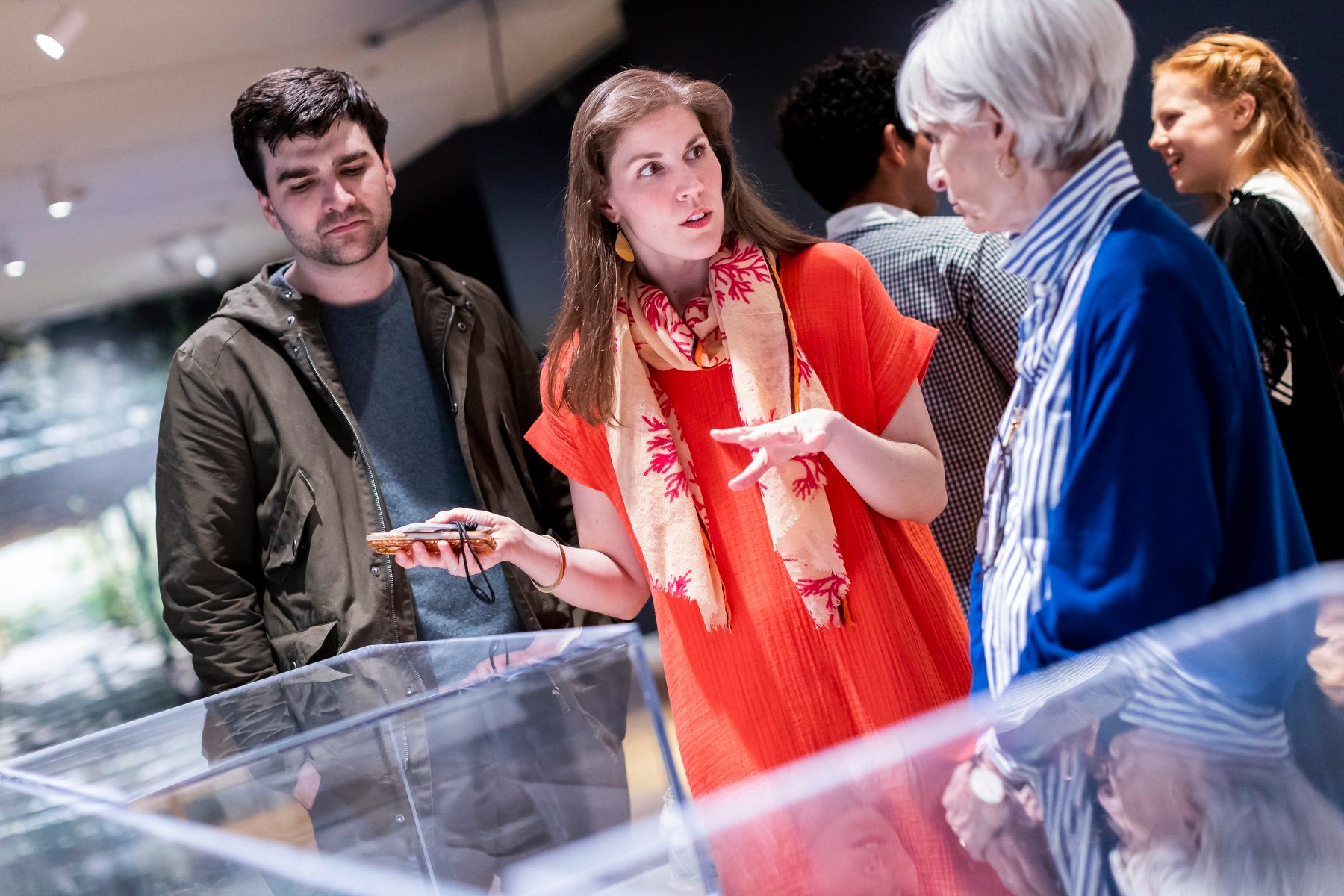 Caroline O’Connell, young woman with brown hair, explains the Design Triennial to an older lady and a young man