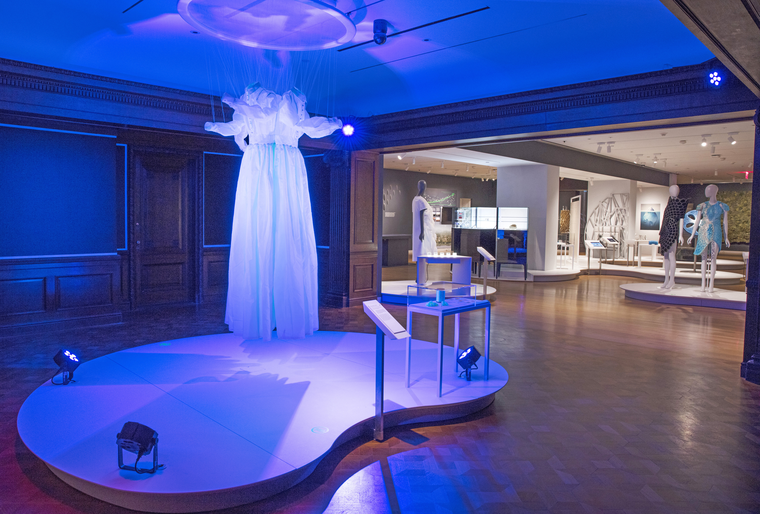 Ghostly prairie dresses, glowing blue, are suspended in the Cooper Hewitt galleries.