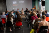 image of a panel discussion at Cooper Hewitt, with audience members looking on and a blonde woman at the podium