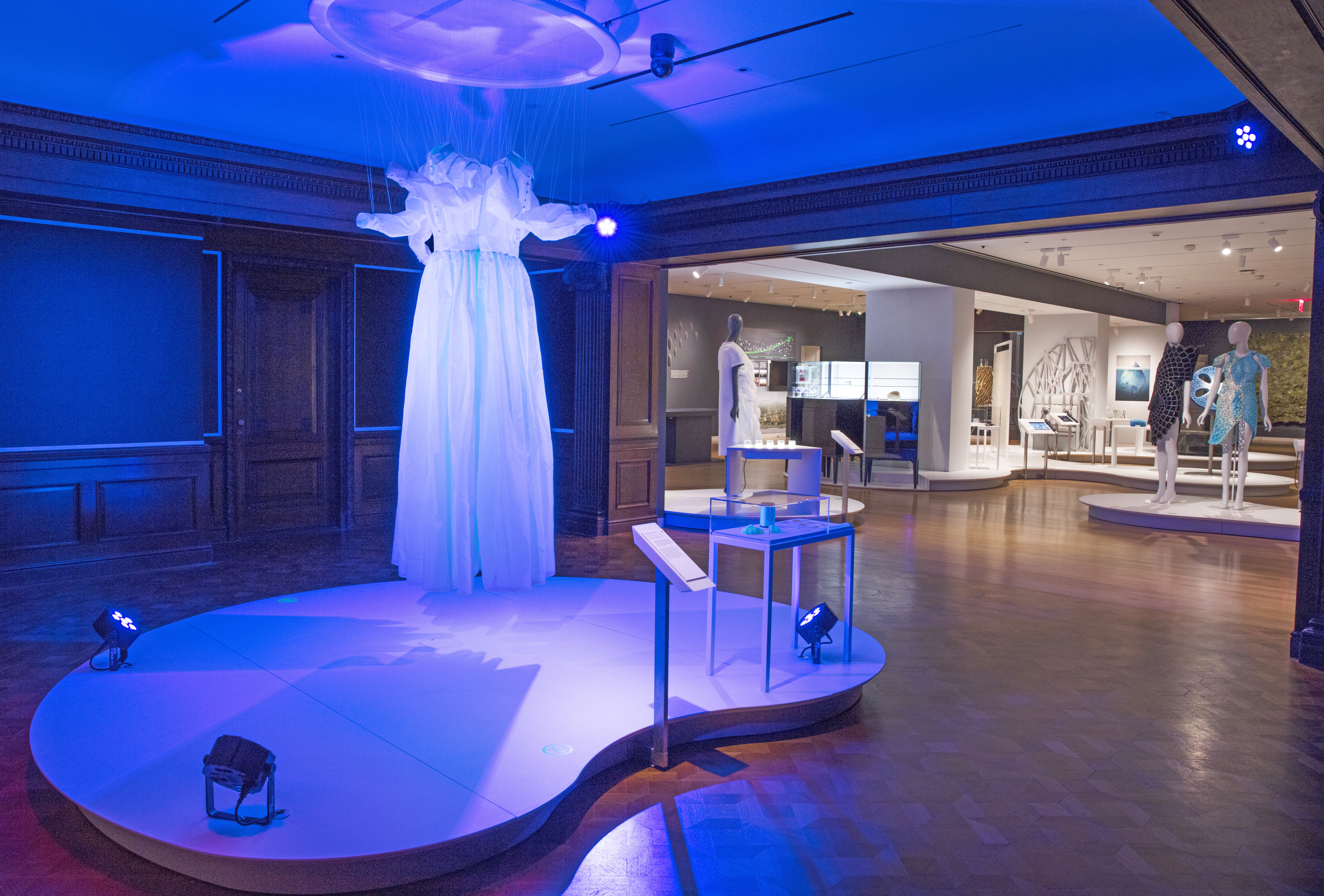 Two conjoined prairie dresses, glowing blue, are suspended from the ceiling.