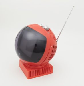 Image features a spherical red portable television with a convex screen at the front, sitting on a square base. Chromed metal control knobs and a chain for hanging and carrying the set are housed in an indentation at the top, with a telescoping antenna to the right. Please scroll down to read the blog post about this object.