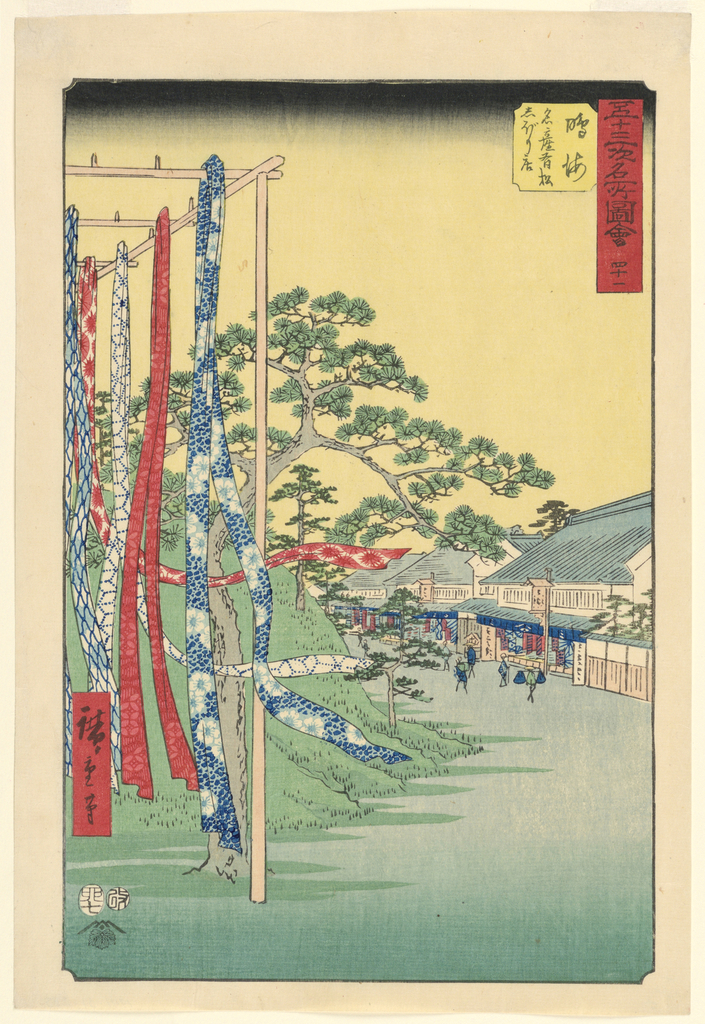 Image features a scene in a town: In the foreground to the left, long strips of colorful fabric hang from wooden poles. In the background to the right, people walk in front of a row of shops under a yellow sky. Please scroll down to read the blog post about this object.
