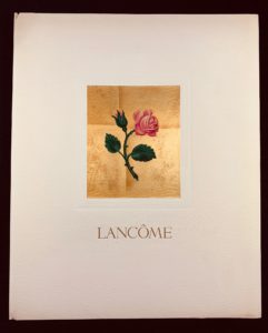 Image features an ivory colored book cover featuring a pink rose on a leafy stem within a gold rectangle in the center. The word LANCÔME in gold capital letters below the gold rectangle. Please scroll down to read the blog post about this object.