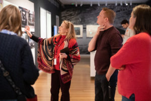 A design guide points to an object on view, engaging visitors in a public tour of an exhibition.