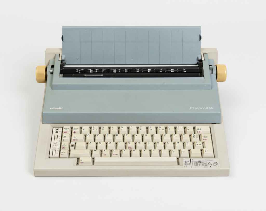 Image features a low, stepped rectilinear typewriter,the; top section and paper support in light blue, yellow knobs on left and right ends of platen, and gray base with gray "QWERTY" keyboard and function keys. Linear indented banding in wedge-shaped base visible in profile.