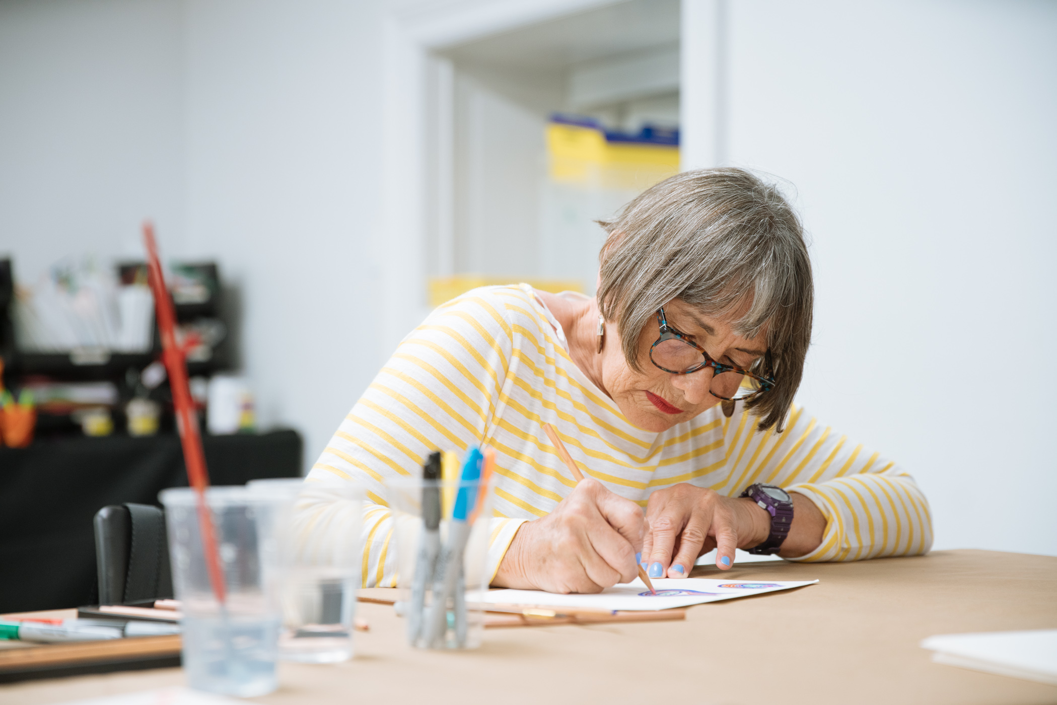 A light-skinned woman with grey hair draws on white paper. Design Dialogue program, scroll down for additional information