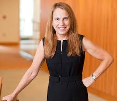 Photograph of Pamela Silver, the other panelist from the Wyss Institute. Pamela has strawberry blond hair past her shoulders. She wears a short-sleeved black dress and has one hand on her hip.