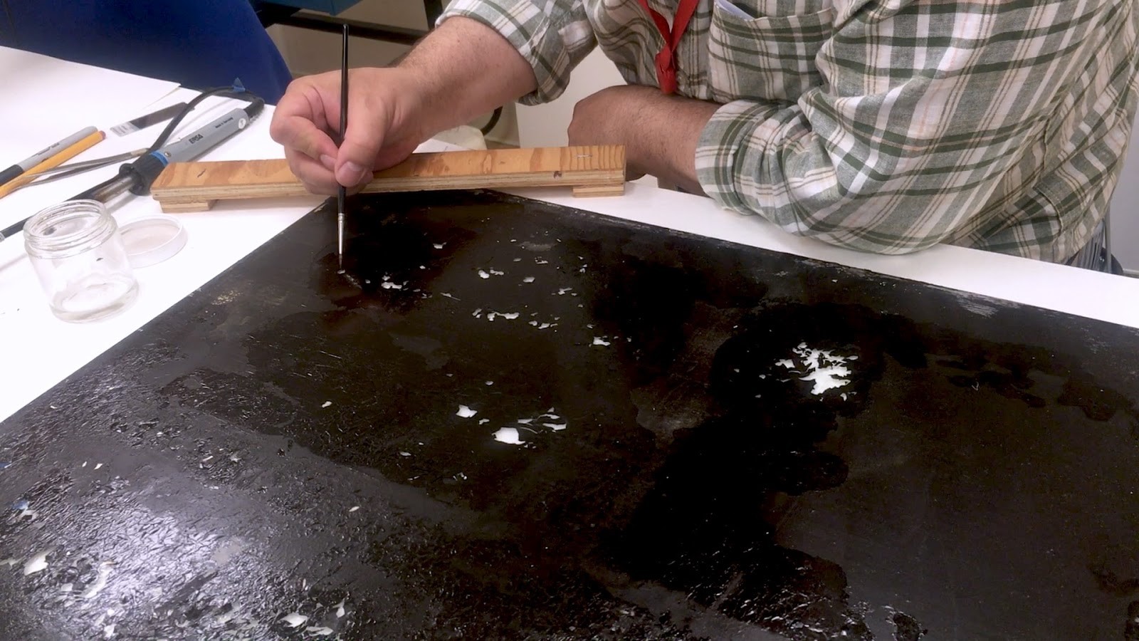 The process of a restoration is being shown with a close up shot of a person leaning over a work desk with paintbrush in hand.