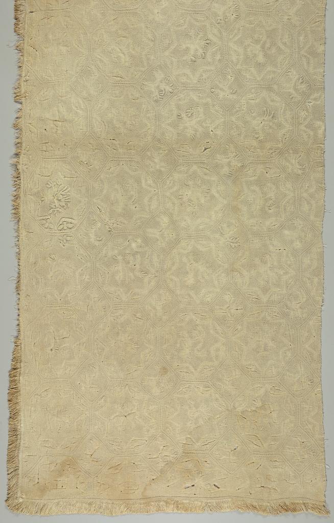 Image features a quilt, the off-white surface with an octagon and diamond grid. Each diamond contains a four-legged animal: one with large antlers, another with a bird perched on its back. Each octagon has an eight-pointed star containing fantastic animals of various types with wings, antlers, tails; some are four-legged and others are bird-like. Please scroll down to read the blog post about this object.