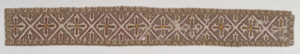 Image features a textile band with a lattice pattern having a cross in each diamond-shaped field. The lattice and crosses are white outlined with red, on a brown ground. Please scroll down to read the blog post about this object.