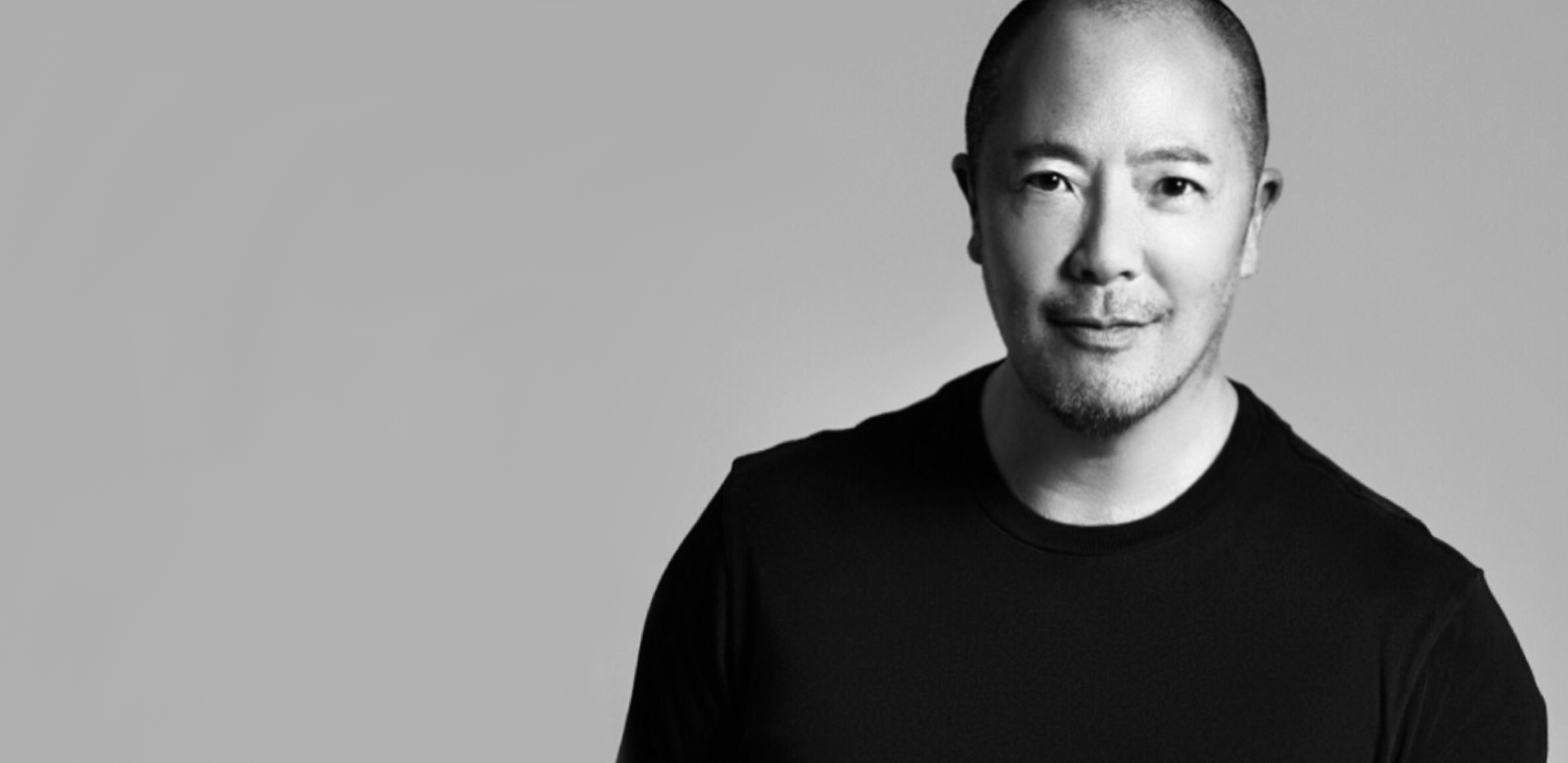 Derek, a forty-something asian-american man with a shaved head, smiles shyly. He is wearing a black tee shirt.